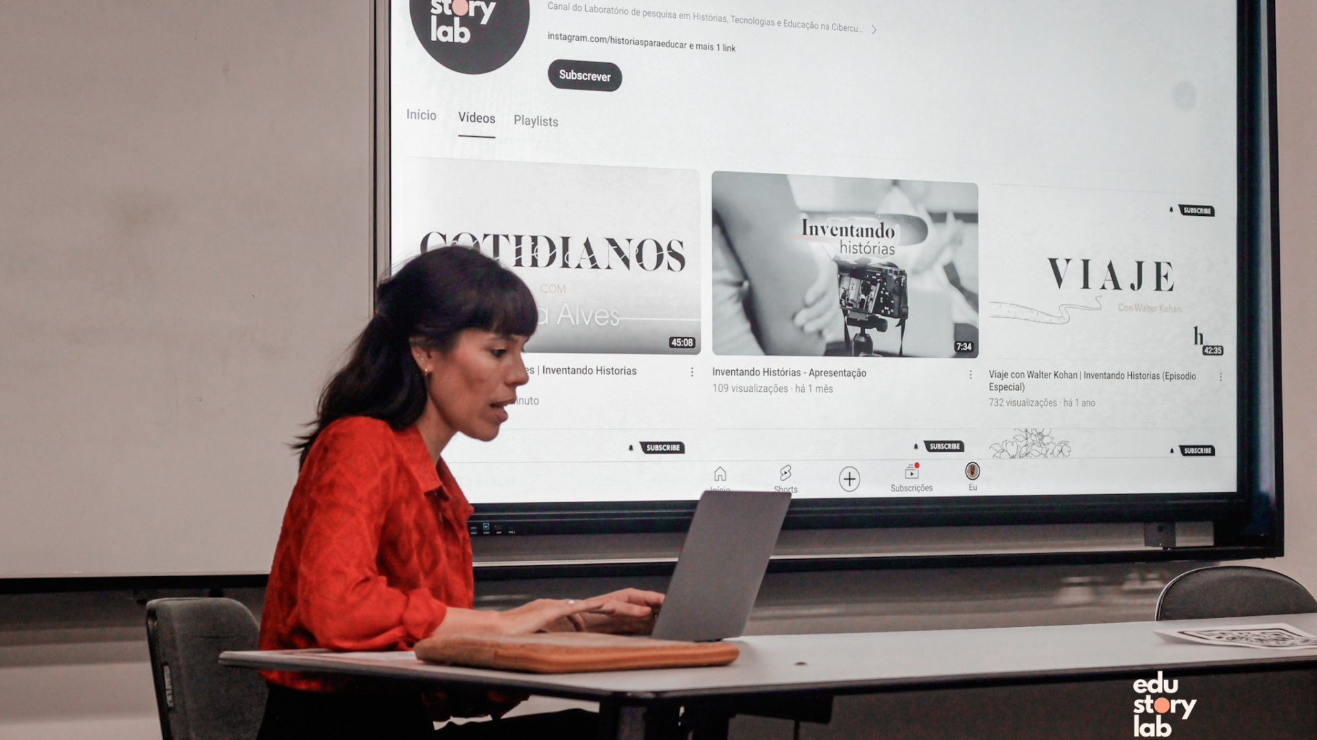 Tania sentada com computador, na sala da UERJ, no dia do lançamento do episódio "Cotidianos, com Nilda Alves".