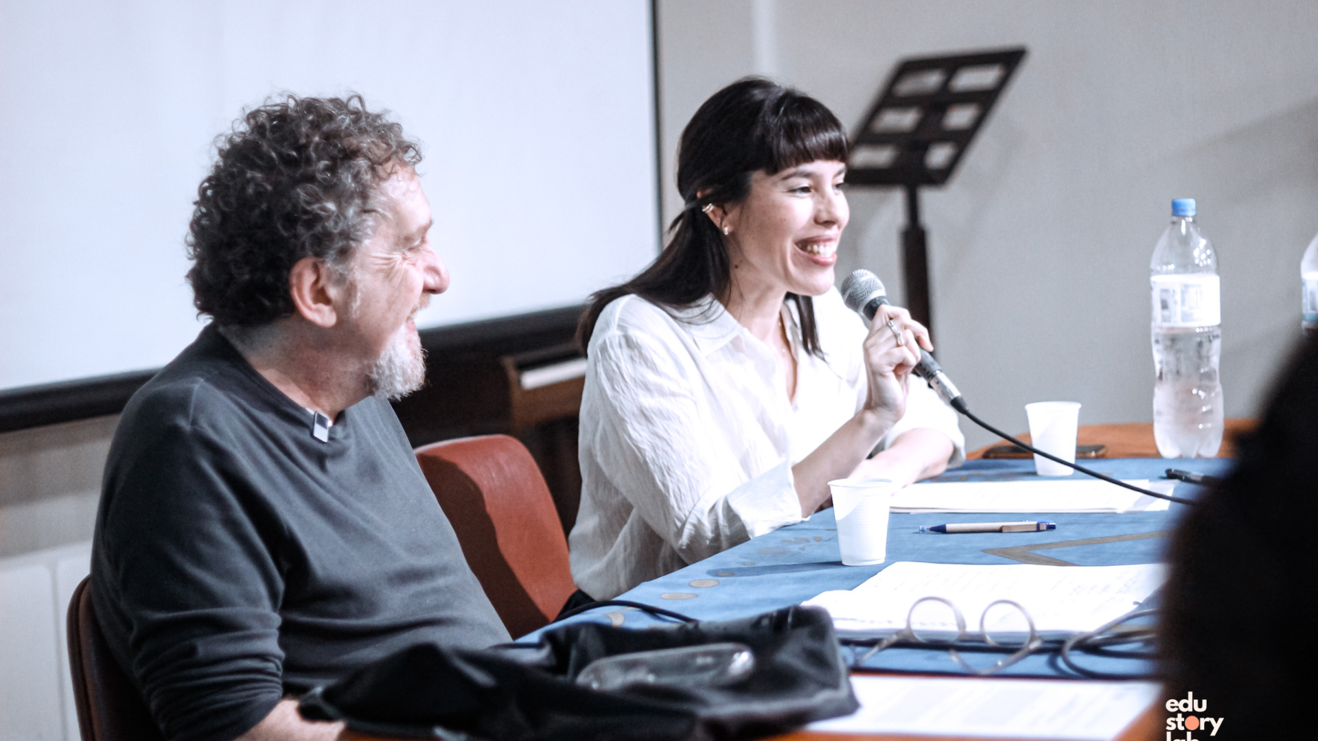 Tania com microfone apresentando a palestra de Carlos Skliar, sentado ao lado, antes de iniciar. UNIRIO